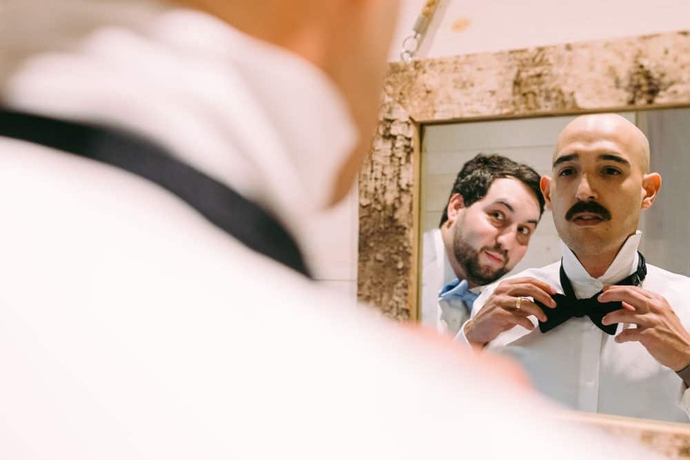 groom adjusting bowtie in the mirror at Wren's Roost Barn