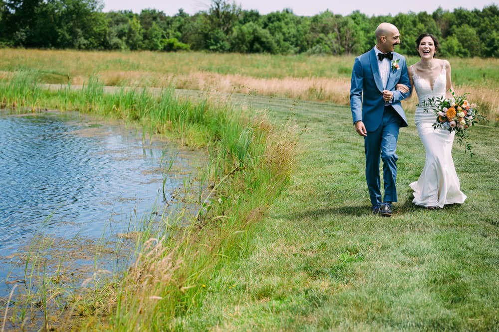 bride and groom walking by the side of a pond at Wren's Roost Barn