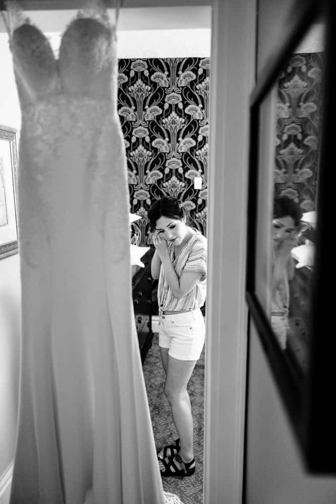 bride getting ready on wedding day with wedding dress in foreground